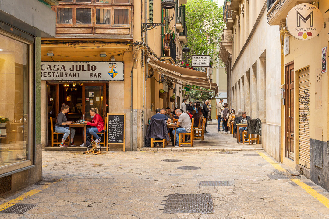 People enjoying their food in a cozy narrow street outside on a terrace in the old town of Palma de Majorca, Balearic Islands, Spain.