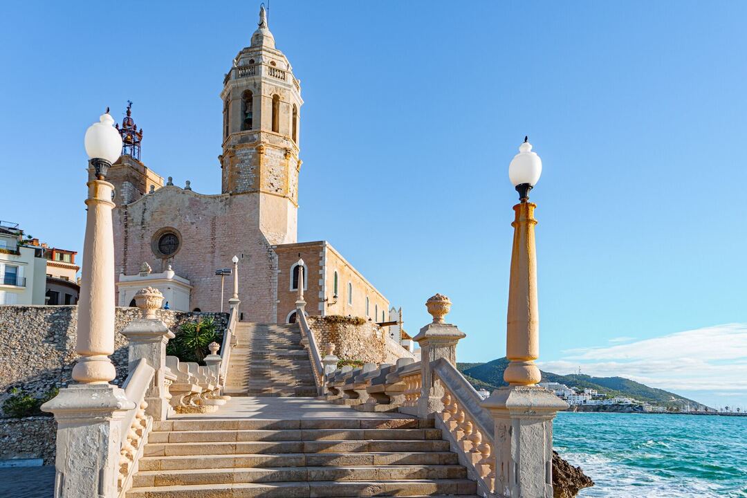 View of stairs leading up to the church of Sitges in Spain, with a blue sky and the sea in the background
