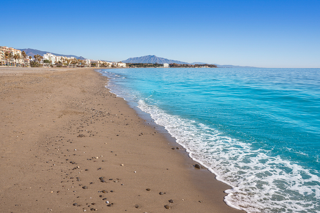 La Rada Beach on a sunny day with turquoise waters, golden sand, and blue sky in Estepona, Province of Malaga, Andalusia, Spain.