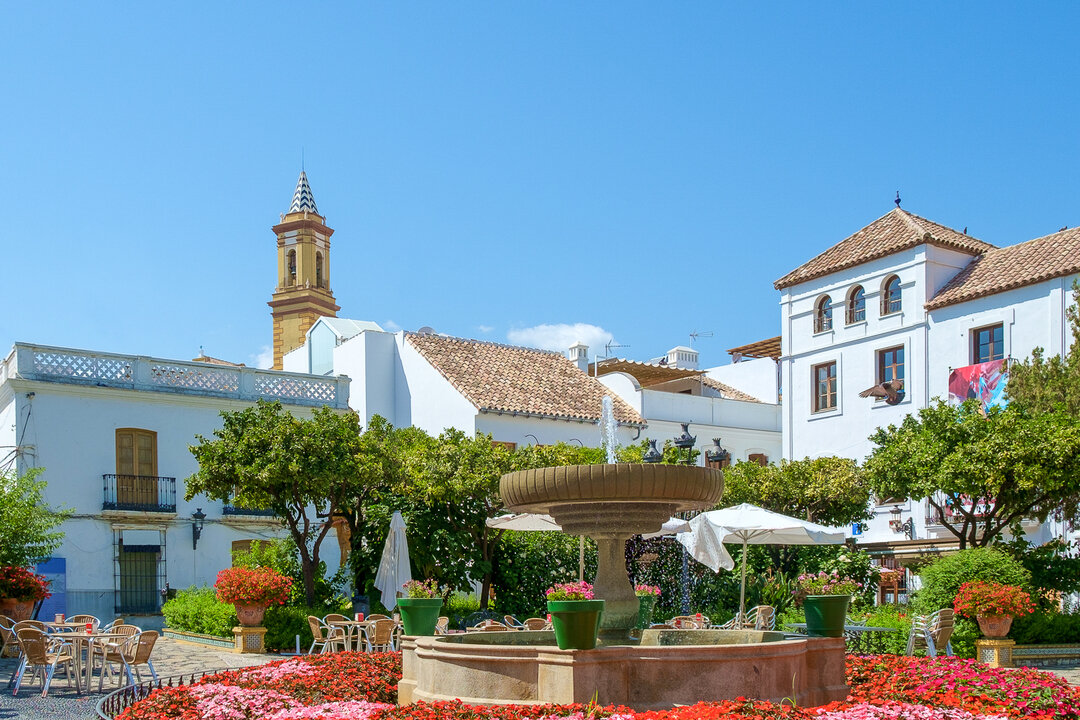 Charming square Plaza de las Flores decorated with colorful flowers, whitewashed buildings, cafés, and a fountain in Estepona, Andalusia, Spain.